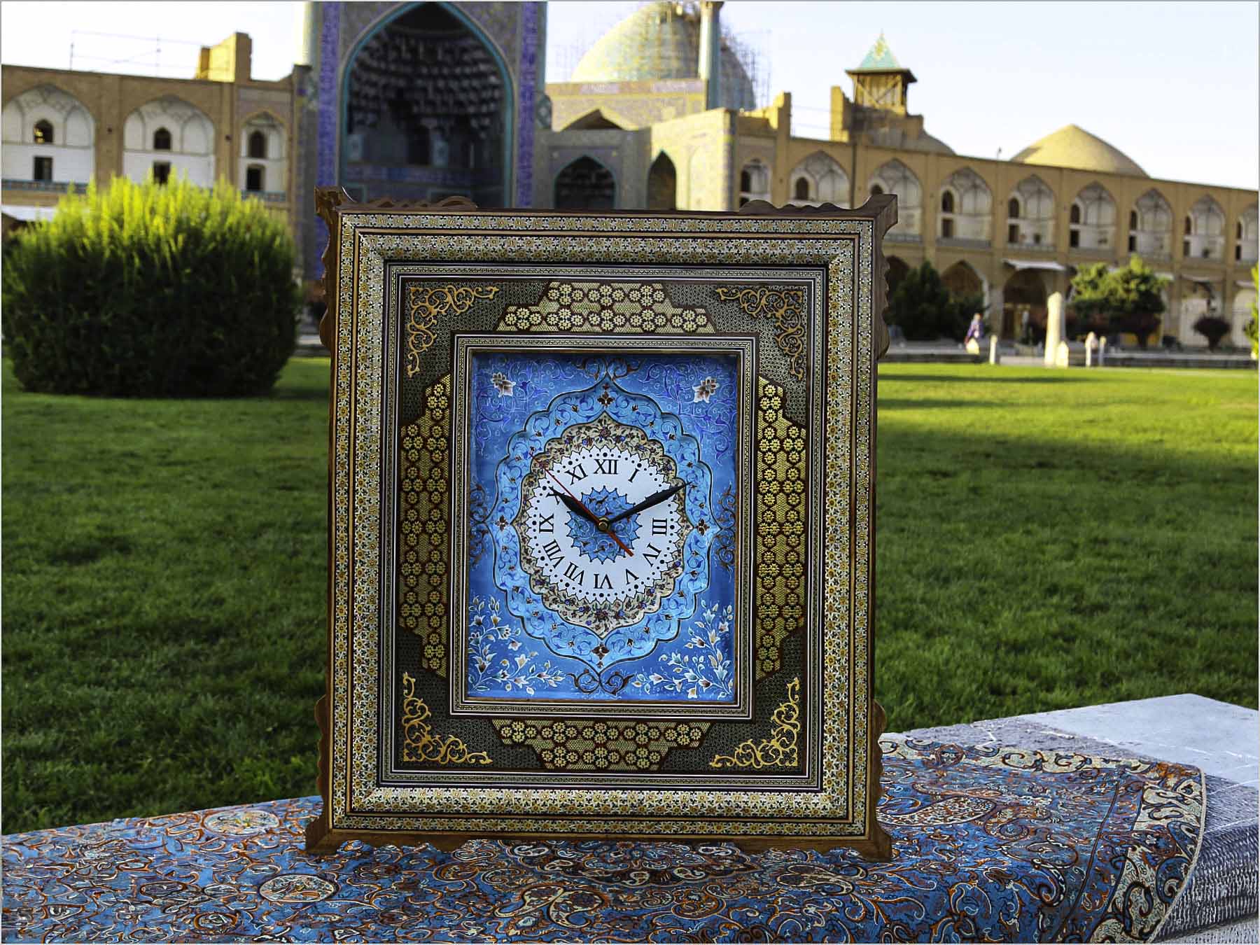 Handcrafted Persian marquetry wall clock with inlaid wooden frame and blue enamel clock face, set in a traditional Persian architectural background.