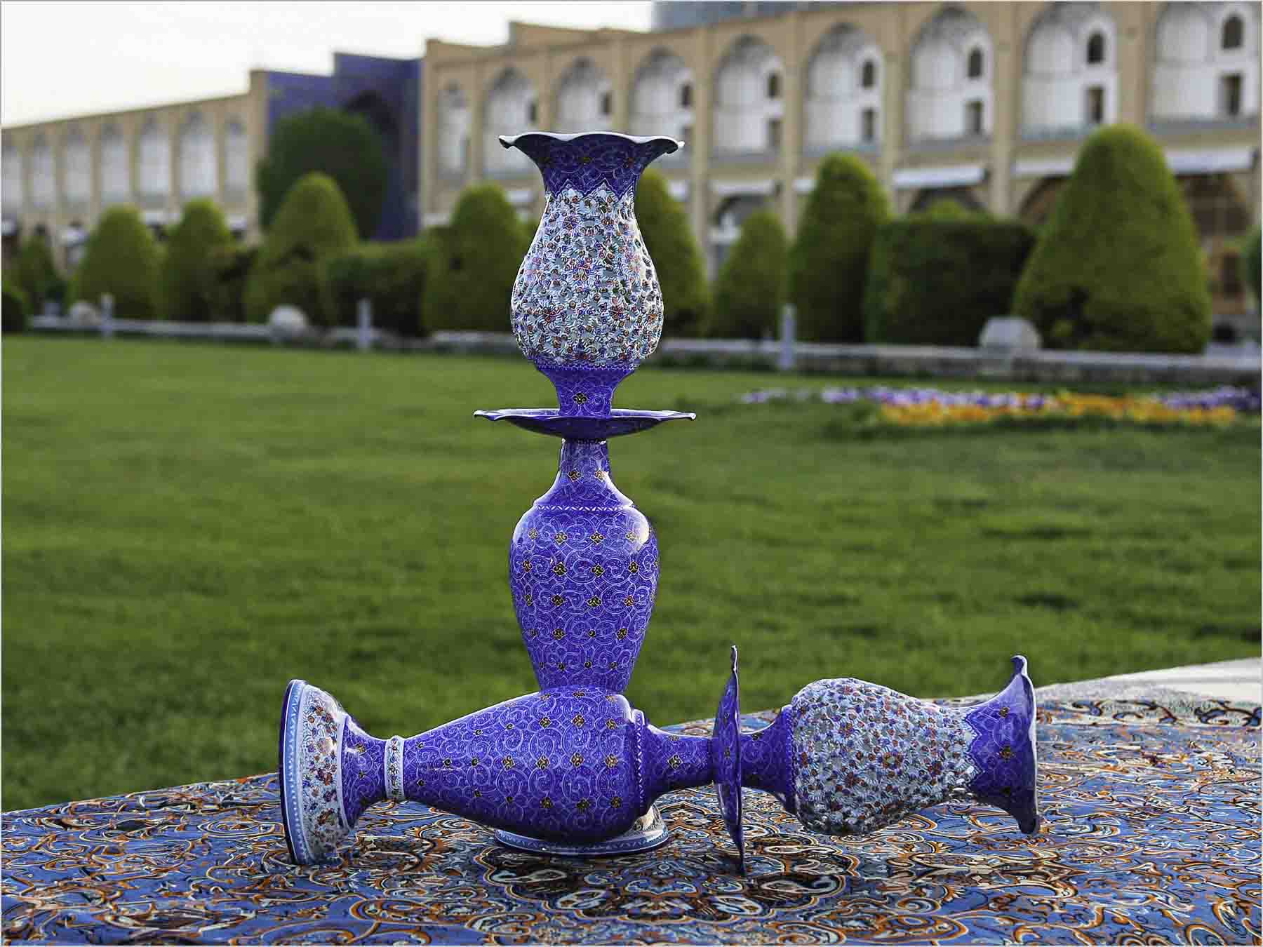 A set of Persian enamel oil lamps with intricate blue and floral designs displayed on a patterned textile outdoors.