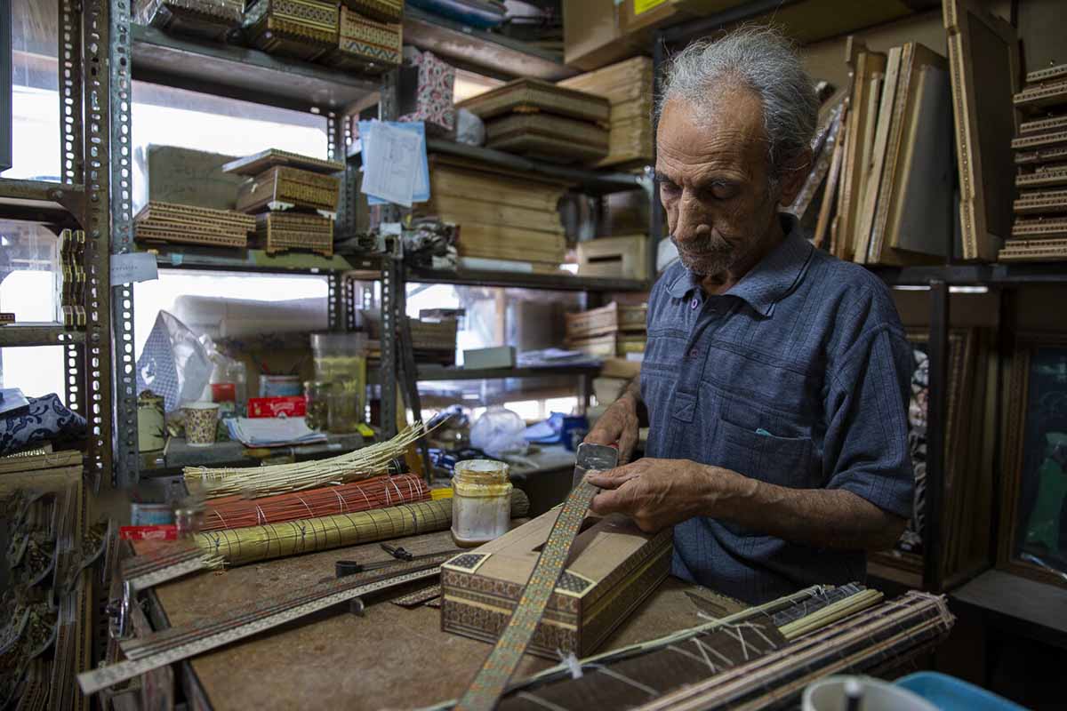 A proud Persian craftsman holds his masterpiece, a beautifully crafted wooden backgammon board. Using the intricate marquetry technique, the wooden pieces are inlaid with intricate designs and patterns, showcasing the craftsman's attention to detail and skill in his trade.