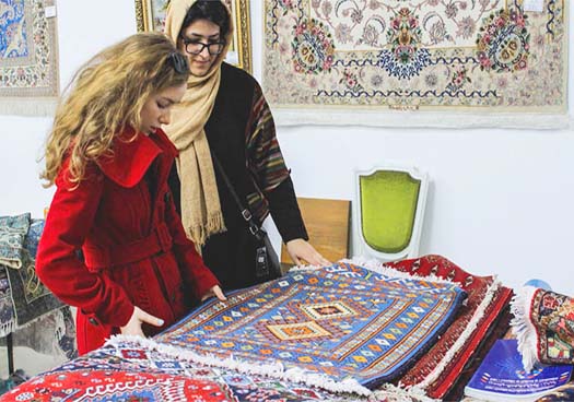 A Persian Woman Shows An Authentic Caltural Persian Carpet To Western Girl In Persian Heritage Carpet Exhibition.
