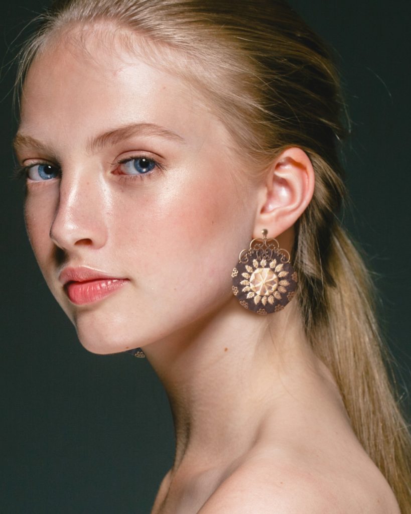 Close-up portrait of a young blonde girl wearing a white circular Balochi Persian embroidery earring.