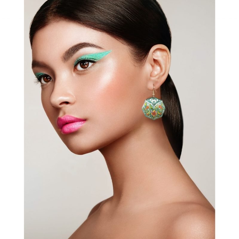 A young woman wearing a pair of Persian Enamelled Green Earrings with a delicate foliage design, made of enamelled copper and silver hooks.