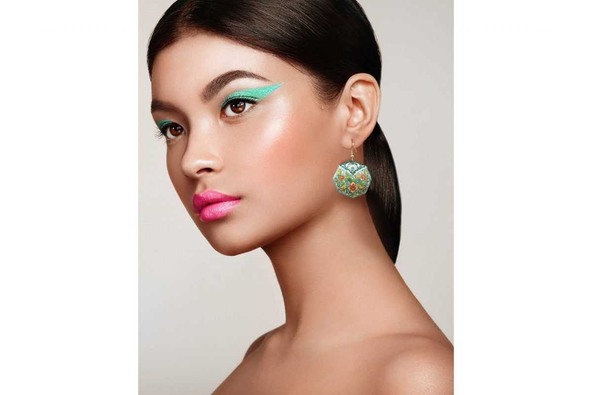 A young woman wearing a pair of Persian Enamelled Green Earrings with a delicate foliage design, made of enamelled copper and silver hooks.