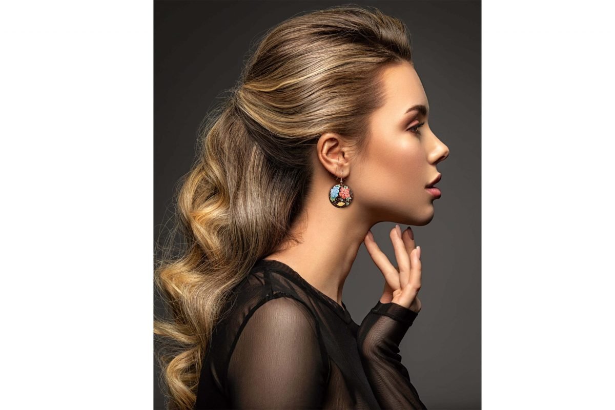 Front view of a beautiful female model wearing Hand-Painted Persian Enamel Watercolour Painting Earrings, featuring a unique Persian garden design in blue, red, and black hues. The earrings are made of enamelled copper with titanium hooks, and each measures 5cm in height and 2.5cm in width.