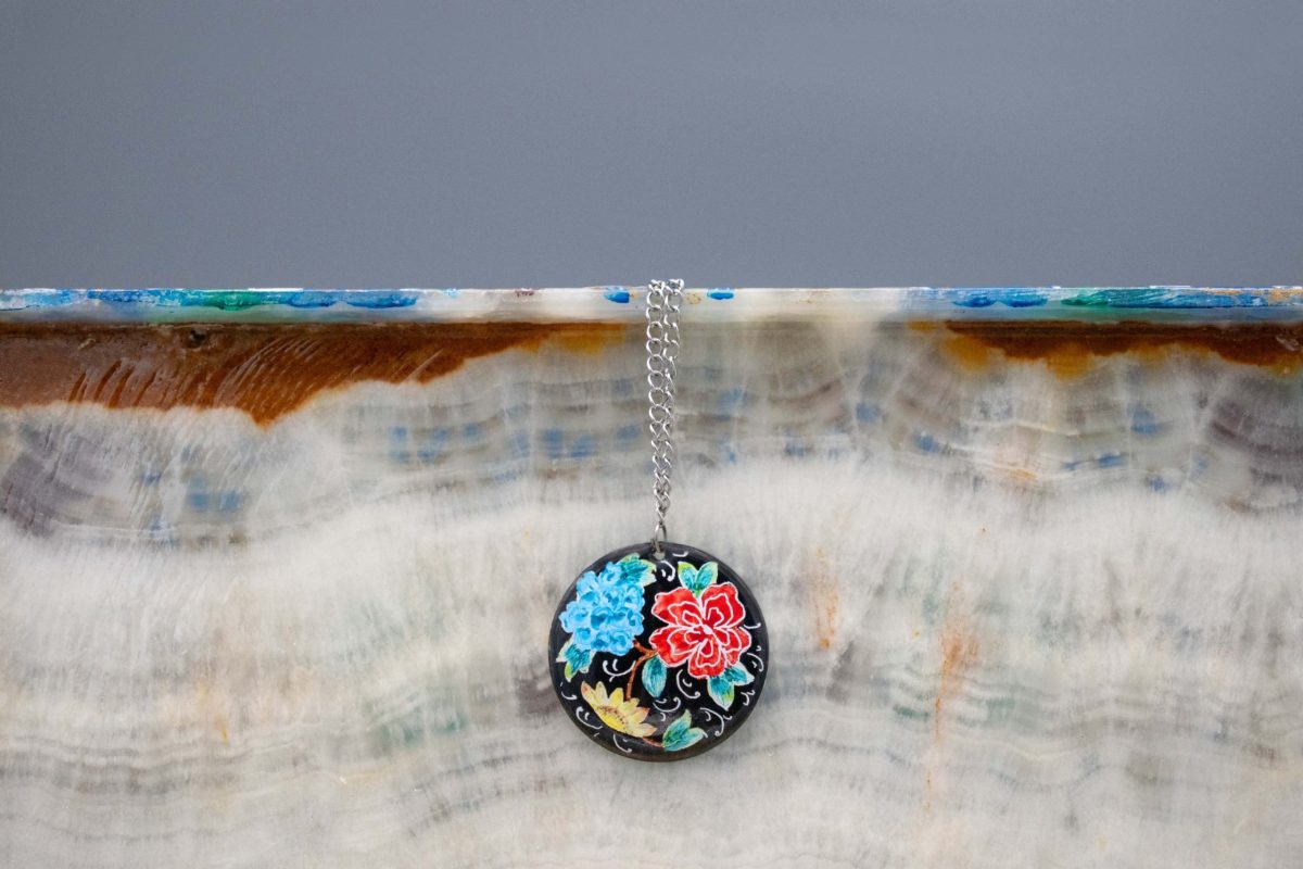 Front view of Hand-Painted Persian Enamel Watercolour Painting Pendant, featuring a unique Persian garden design in blue, red, and black hues. Made of enamelled copper with a titanium chain. The pendant measures 7cm in height and 5cm in width.