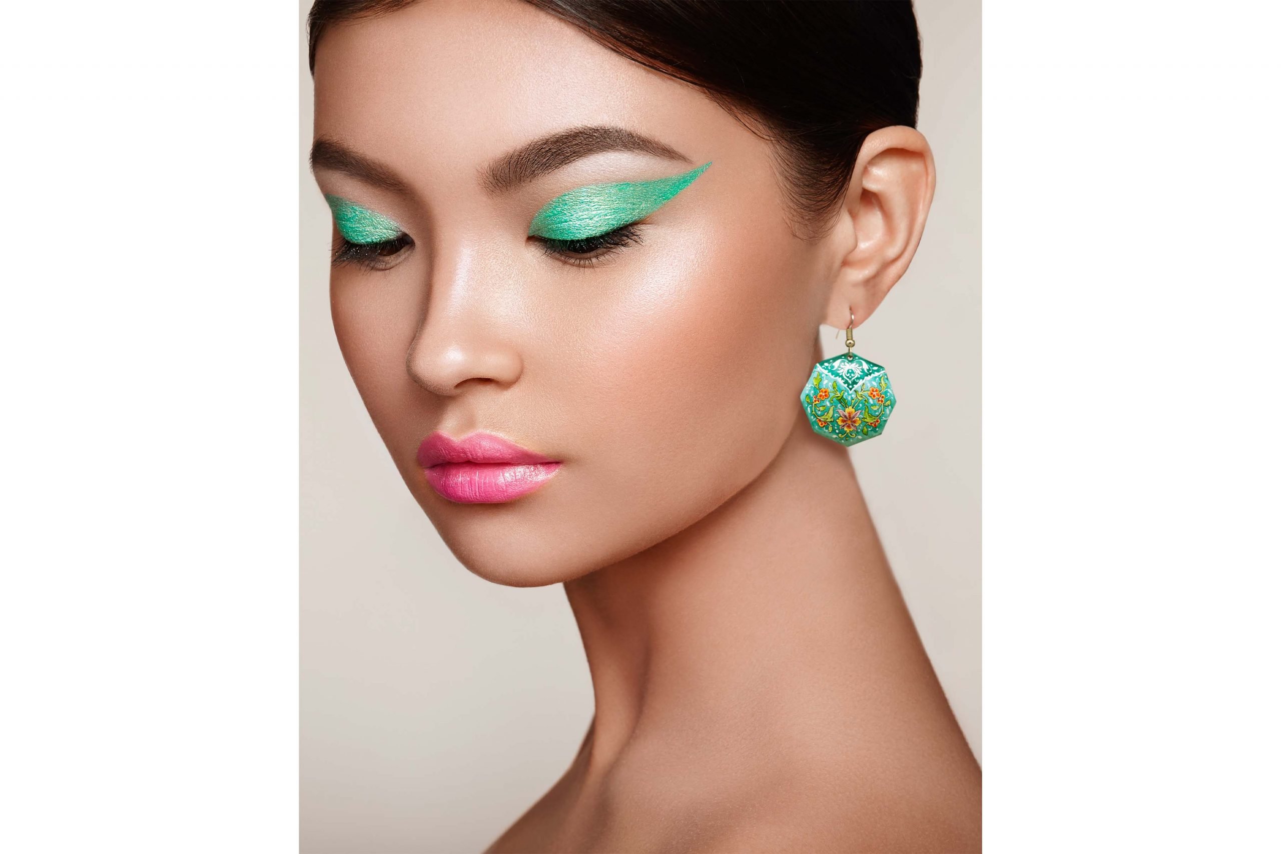 A young woman wearing a pair of viridescent enamel earrings with a delicate foliage design, made of enamelled copper and silver hooks.