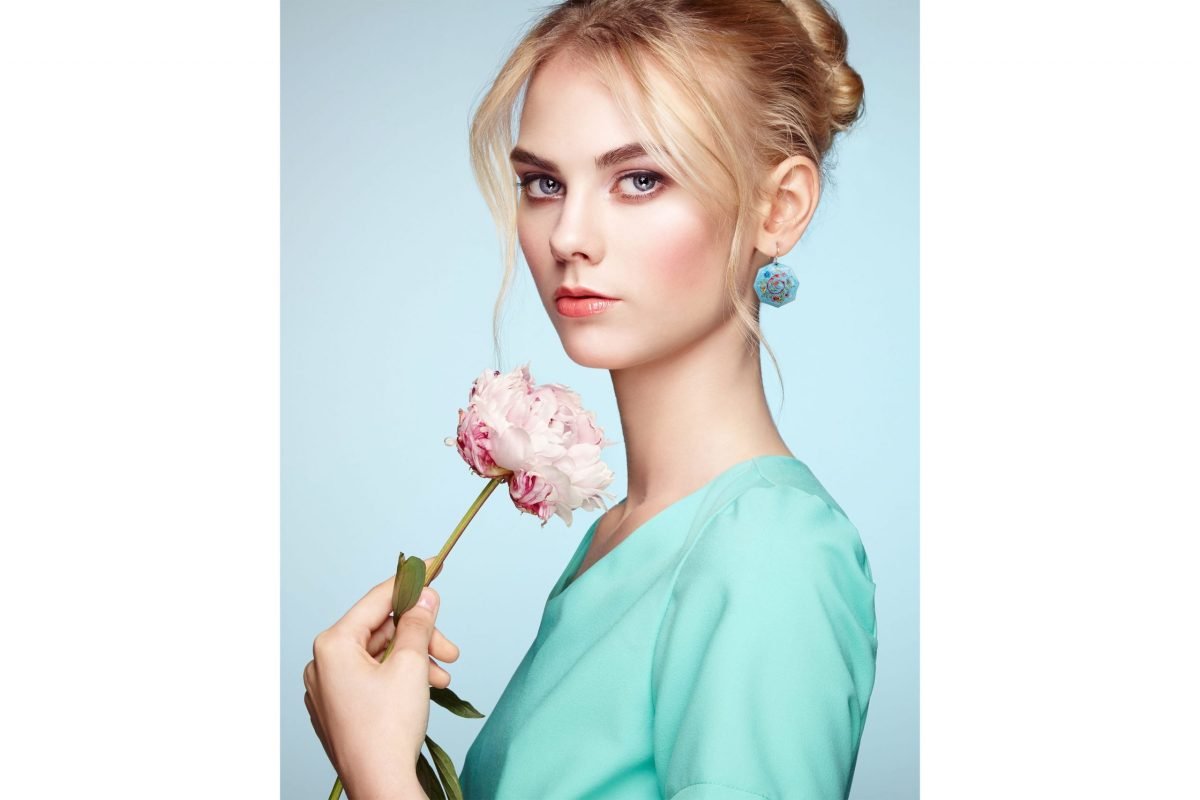A beautiful girl wears a pair of enamelled earrings from The Exquisite Hand-Painted Jewellery Set while holding a matching flower. The intricate design features iconic foliate and foliage symbols, combining modern, retro, and artistic styles.