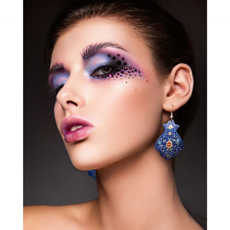 A portrait of a beautiful girl wearing Blue Persian Enamel Watercolour Painting Earrings, featuring a hand-painted Persian garden design on an enamelled copper body with a titanium hook.