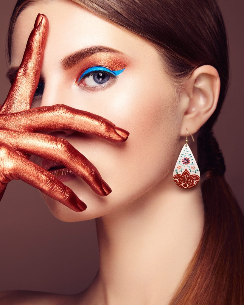 A portrait of a beautiful girl wearing drop-shaped Persian jewellery featuring intricate hand-painted floral designs in white and crimson, adding a touch of sophistication to her overall look.