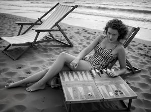 A woman on the beach playing backgammon, representing Persian backgammon and its cultural significance