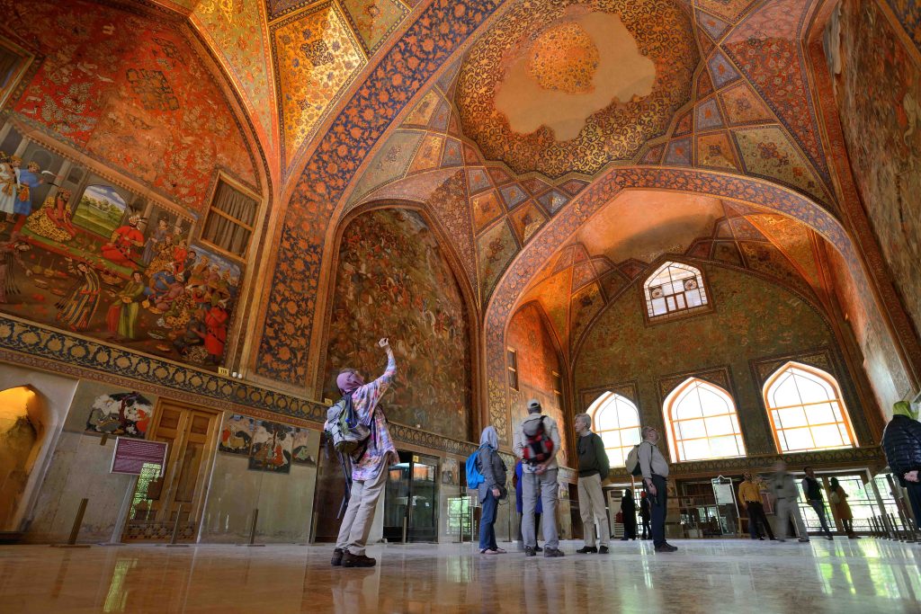 Interior of the Chehel Sotoun palace in Isfahan, Iran, featuring tall columns, vibrant frescoes, and elegant carpets.