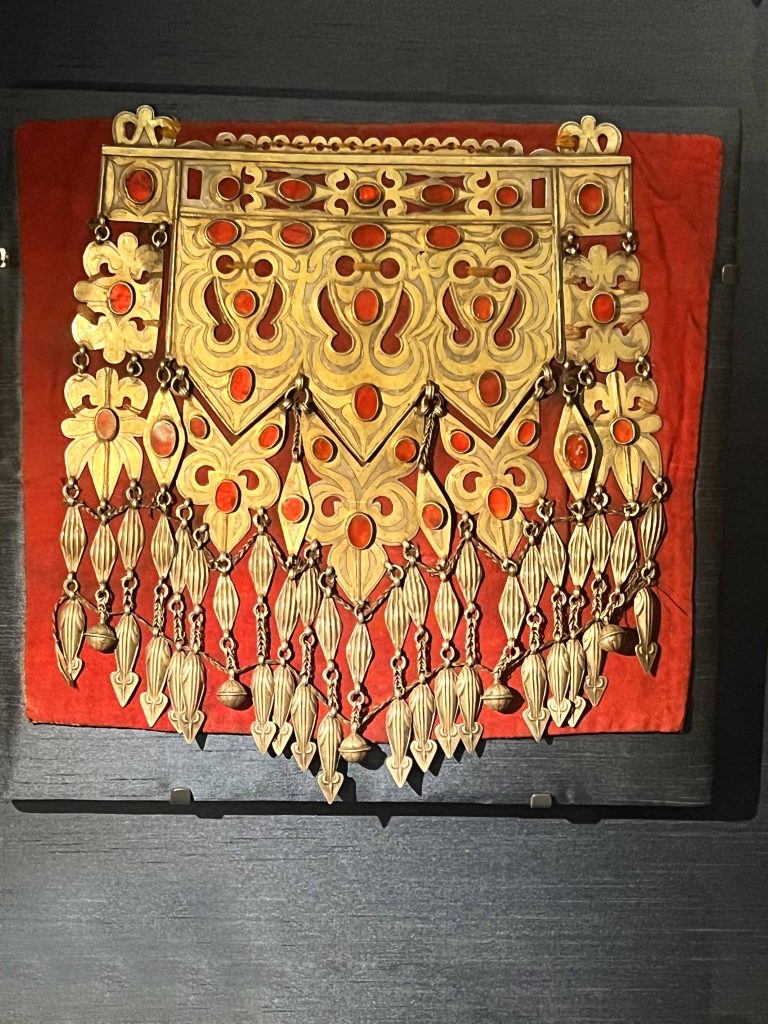 An intricately designed Turkmen curved crown on display in the British Museum. Keywords: Turkmen, earrings, cultural heritage, wealth, status, natural world, Silk Road, traditional design, contemporary design, craftsmanship.