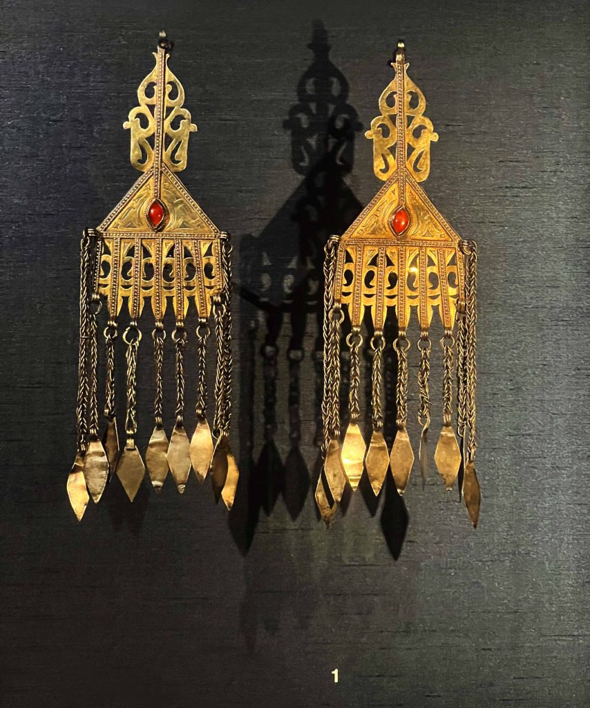 A pair of intricately designed Turkmen earrings on display in the British Museum. Keywords: Turkmen, earrings, cultural heritage, wealth, status, natural world, Silk Road, traditional design, contemporary design, craftsmanship.
