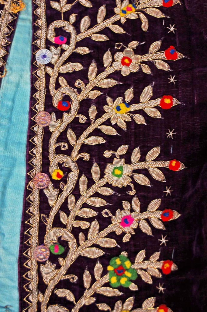 Purple velvet jacket lined with light green glazed cotton, featuring metal thread embroidery and colorful woolen bobbles.