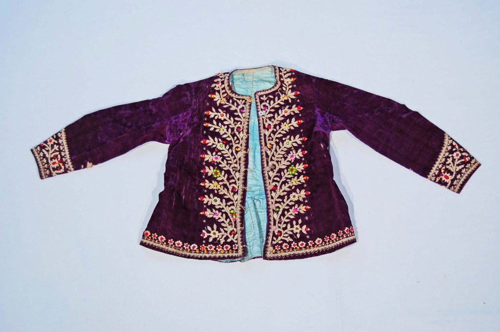 Purple velvet jacket lined with light green glazed cotton, featuring metal thread embroidery and colorful woolen bobbles. Persian fashion history.