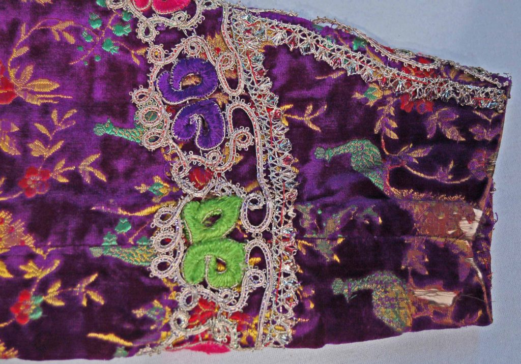 This exquisite purple velvet jacket features intricate woven designs of peacocks and colorful flower sprays, showcasing the vibrant artistry of Persian textiles. The jacket is further enhanced with embroidered and couched designs along the front edges, hem, collar, and cuffs, creating a striking visual appeal. Acquired in Iran, this jacket represents the rich cultural heritage and skilled craftsmanship characteristic of traditional Iranian attire.