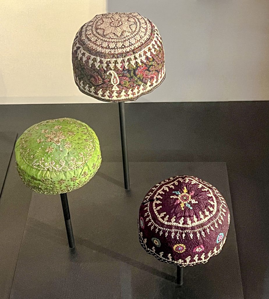 Embroidered caps, one in purple silk and the other in termeh wool fabric, showcasing intricate buttonhole stitch embroidery and cultural symbolism from Azerbaijan or northwestern Iran. Persian fashion history