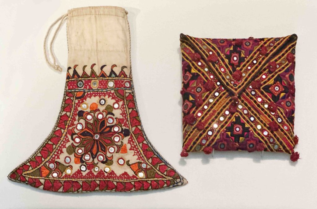 A photo of embroidered storage bags and purses from Baluchistan, showcasing cream-colored bags traditionally used by bridegrooms to store tobacco, betel nut shavings, or small gifts for wedding ceremonies, and envelope-shaped bags gifted to brides by female relatives for storing Qur'ans or mirrors. The intricate embroidery adds both visual appeal and cultural significance to these functional items.