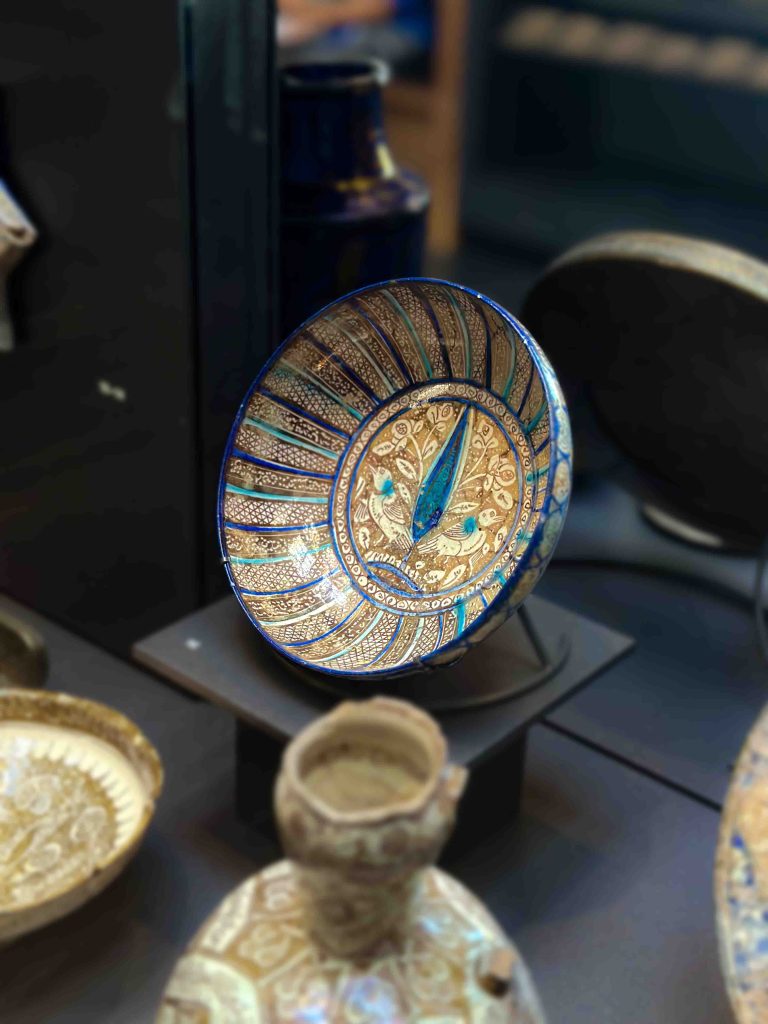 A stunning Ilkhanid bowl crafted from stonepaste, painted with lustre, blue, and turquoise decorations, featuring a bird and foliage motif, palmette motifs, and inscription.Khata'i Persian Art
