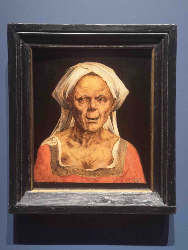 Image of Quinten Massys' painting 'An Old Woman', featuring a modestly dressed elderly woman with expressive features.