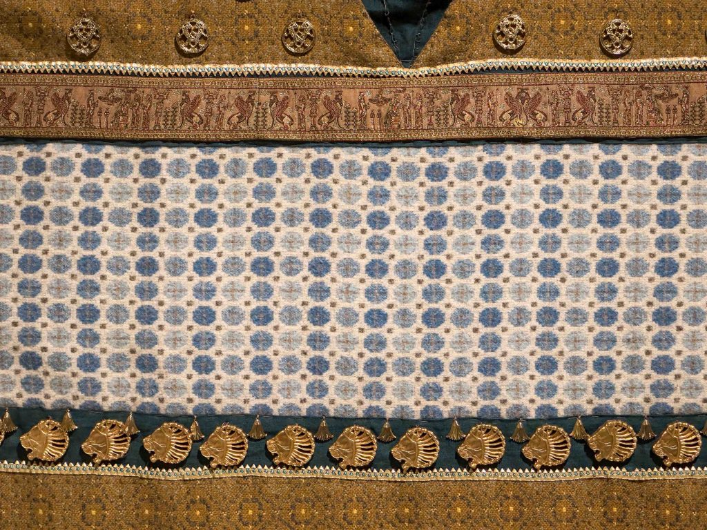 An image of the meticulously recreated Achaemenid royal costume, adorned with intricate metallic embroidery and gold-painted resin appliqués on luxurious lamb's wool, offering a tangible glimpse into the magnificence of ancient Persian court attire.