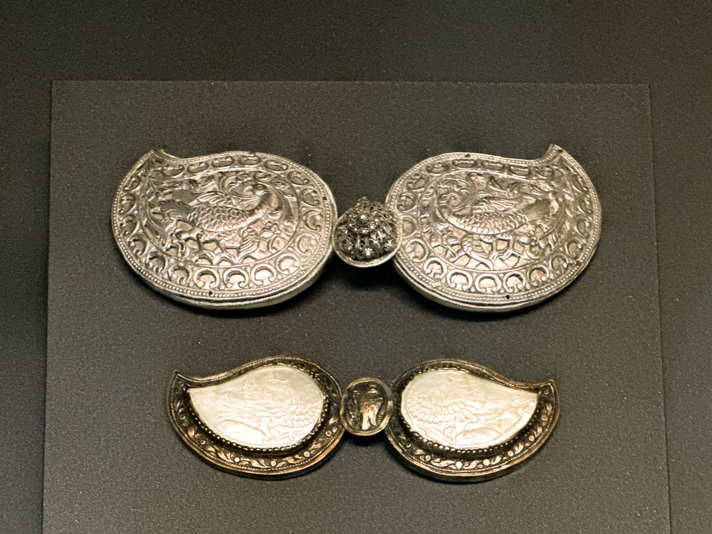 Two intricately designed Ottoman-era belt clasps. One in nickel silver with a peacock motif, the other in copper alloy adorned with mother-of-pearl bird engravings.