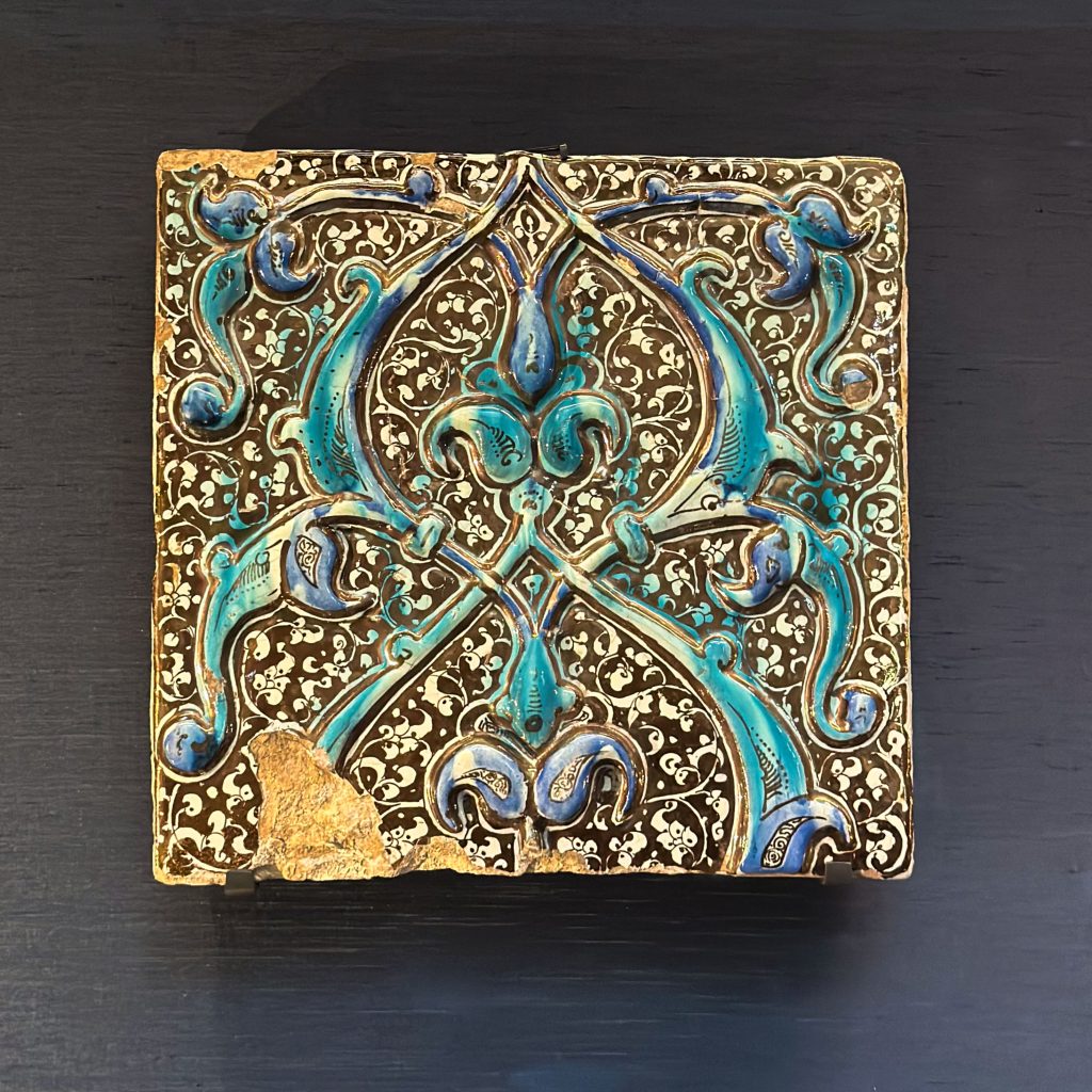 A rectangular stonepaste frieze tile from Kashan, decorated with blue and turquoise split-palmette scrolls against a shimmering lustre background, embodies the evolution of techniques in the history of enamelling