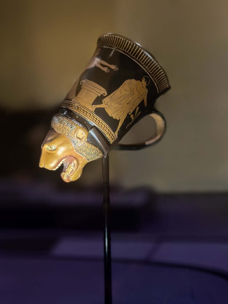 An intricately detailed red-figured handled rhyton showcasing a harmonious blend of Persian opulence and Greek innovation, with vibrant depictions symbolizing strength, nobility, and cultural unity, illustrating the mutual influence and shared aesthetic values of both civilizations.