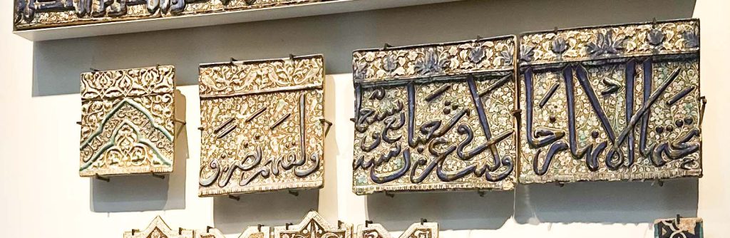 1308 circa Ilkhanid frieze tile with Qur'anic inscription, paired birds, and dense foliage design in blue, turquoise, and lustre, exhibited at the British Museum. Persian Tile Artistry