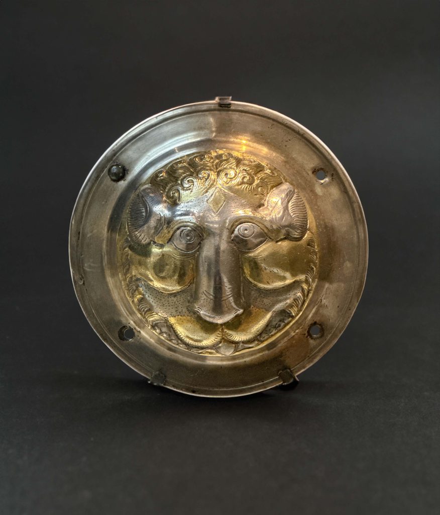 Silver gilt shield boss with a detailed Persian lion's face, accentuated with gold touches on the mane, cheeks, and upper lip, hailing from the Early Sasanian period in Iran.