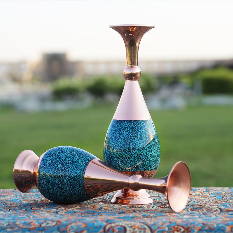 A 30 cm Sarahi Turquoise Inlay Vase crafted from Kerman copper, featuring an elongated design and adorned with hand-set Nishapur turquoise stones in a mosaic pattern.